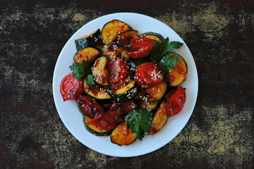 Baked zucchini slices with cherry tomatoes and sesame on a white plate. Vegan dinner Diet food.