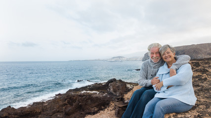 Fototapeta premium One senior couple of people waiting the sunrise sitting on the cliff and looking at camera. Early morning for two retired person in holiday at sea