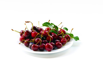 Obraz na płótnie Canvas red cherries and leaves in a white plate on a white background
