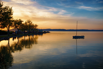 Beautiful sunset over lake Balaton with silhouettes of a sailboat, and a pier with trees in Hungary