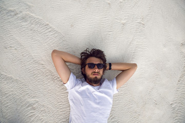 man with a beard in a white t-shirt and shorts rest on a white mountain