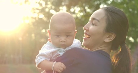 Mother playing with baby at park. Young asian mother holding her baby son aloft in park or garden with happy emotion. Slow motion. - Powered by Adobe