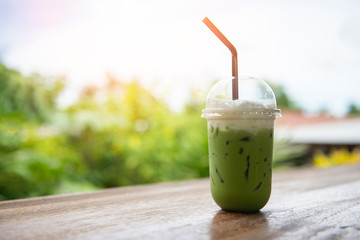 iced green tea in plastic cup / matcha green tea latte frappe and straw on wooden table with nature