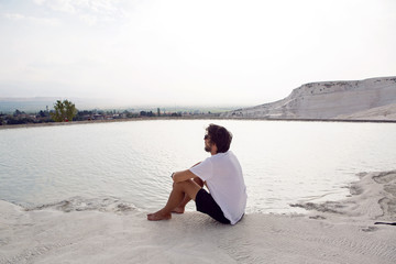 man with a beard in a white t-shirt and shorts sitting on a white mountain