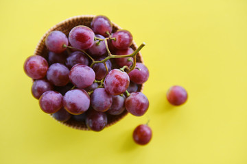 Red grape bunch in basket - Fresh grape fruit on the table with yellow background