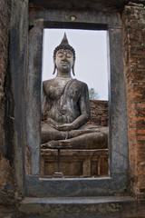 Obraz premium view through the frame on seated Buddha statue in famous Sukhothai Historical Park, a UNESCO World Heritage Site, the ancient 13th and 14th centuries capital of Sukhothai. Thailand