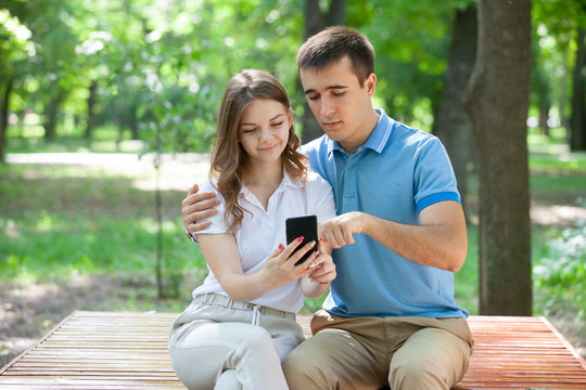 Couple sharing media in a smart phone sitting in a bench in a park.