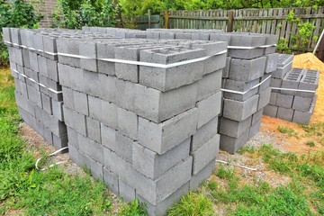 Stack of gray textured cinder blocks for house or fence building. Construction Materials. Pallet with cinderblocks and pile of sand on background. Row of grey concrete bricks. Brickwork 
