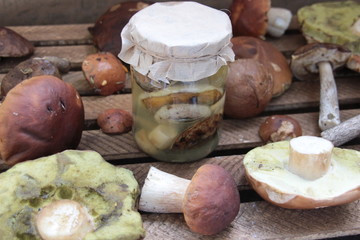 Fototapeta premium Marinated canned mushrums in glass pot on wooden background with fresh white mushrooms, boletus