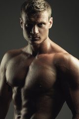 Fototapeta na wymiar Bodybuilding and body sculpture concept. Beautiful (handsome) muscular male model with blond hair, perfect body posing over gray background. Close up. Studio shot