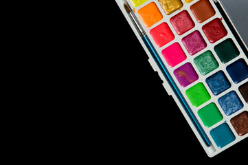 Close up, flat lay. Stationery. A palette of multicolored watercolor. Isolated on black background. Copy space.