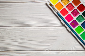 Close up, macro, flat lay. A palette of multicolored watercolor. White wooden background. Copy space.