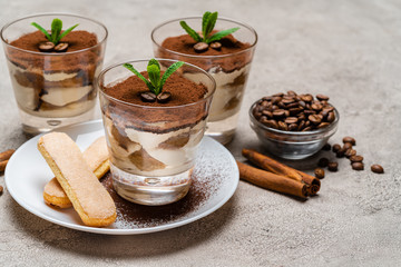 Classic tiramisu dessert in a glass cup and savoiardi cookies on plate on concrete background