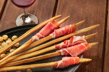 Prosciutto-wrapped Italian grissini with red wine and roasted almonds, close-up shot on a wooden...