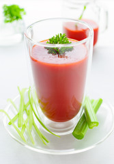 a glass of organic tomato juice with parsley and celery on white table