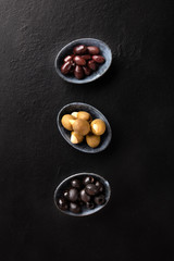 Various types of olives in bowls, shot from the top on a black background. Purple, green almond stuffed, and black pitted olives