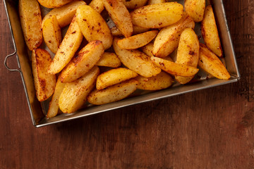 Potato wedges, oven roasted, close-up shot from above in a baking tray on a dark rustic wooden background with a place for text