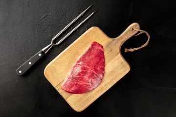 Kobe meat, wagyu beef steak, raw, overhead shot with a carving fork on a black background with copy space