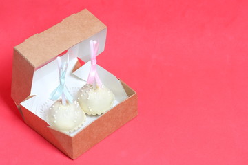 Cake pops decorated with a bow of braid, packed in a gift box. Against the background of coral color.
