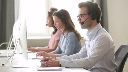 Focused male call center agent in wireless headset helping customer - Powered by Adobe