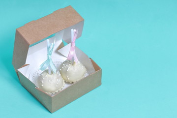 Cake pops decorated with a bow of braid, packed in a gift box. Against the background of mint color.