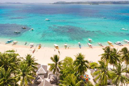 Daco island, Philippines. Palm trees and bungalows on the white sandy beach. People relax on a tropical island,view from above.