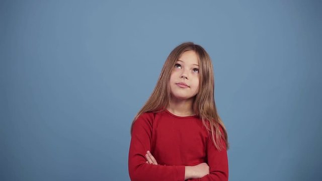 Cute long haired girl in red sweater disapproving with No hand sign, make negation finger gesture. Denying, rejecting, disagree. Portrait of beautiful little girl. Slow motion over blue background