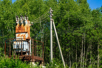 Transformer substation is installed on concrete supports in forest glade. Close-up. Cables from existing power line are connected to substation through ceramic insulators.