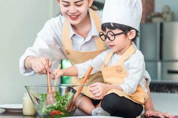Mom and his little daughter cooking bolognese sauce for salad in the kitchen, there is steam escaping from the pan on cooking plate