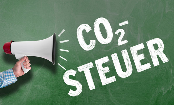 hand holding megaphone or bullhorn against blackboard with text CO2-STEUER, German for carbon tax, climate protection concept