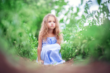 The little girl in a blue sundress sits in a plantation of tomatoes and longs