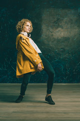 Obraz premium A young guy with a surfer's hair in a yellow jacket and headphones is dancing against a dark background