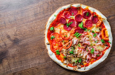 Pizza "Four Seasons" with Mozzarella cheese, ham, tomato sauce, salami, bacon, mushroom, pepper, Spices and Fresh basil. Italian pizza on wooden table background