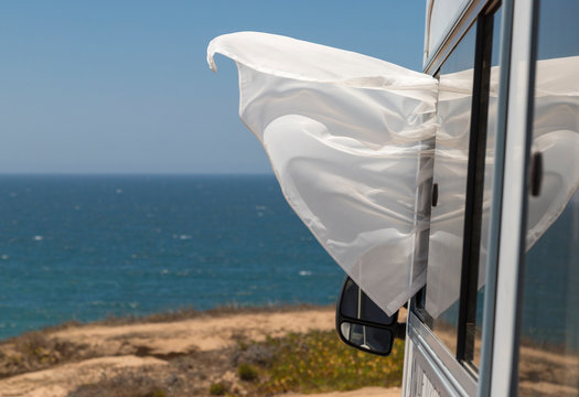 Una cortina de una autocaravana vuela por una ventana con el fondo del oc&eacute;ano atl&aacute;ntico, en la costa portuguesa