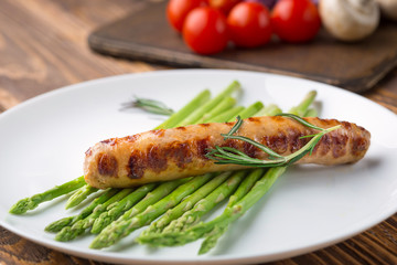 Fried sausage with asparagus on a white plate, wooden table.