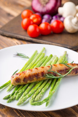 Fried sausage with asparagus on a white plate, wooden table.