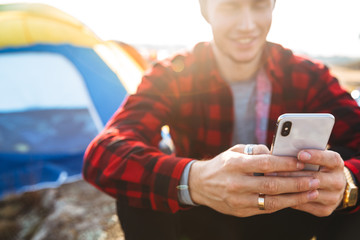 Man outside in free alternative vacation camping over mountains using mobile phone chatting.