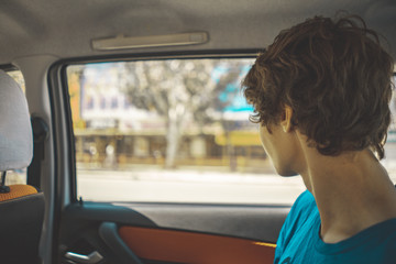 young teenager sitting on the back seat of the car and looking through the window