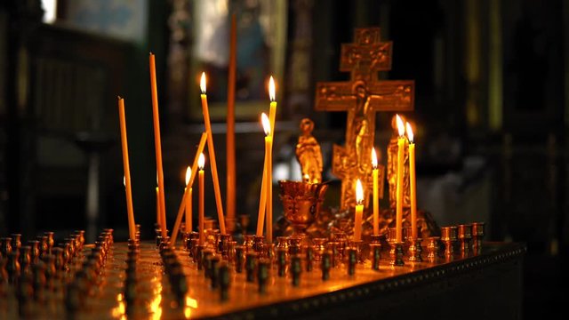 Large gold candlestick with burning candles in the form of a table with many cells for candles and a small crucifix, against the dark room of the Orthodox Church