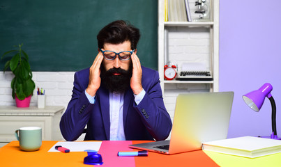 Bearded teacher near chalkboard in school classroom. Professor in class on blackboard background. Back to school. World teachers day. Learning and education. Tired male university student at table.