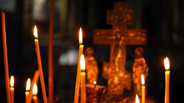 Many burning candles close-up against the blurred Golden crucifixion of Jesus Christ in a dark room of the Orthodox Church