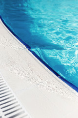 Blue water with light reflection at the edge of the curved swimming pool. The concept of summer travel and recreation