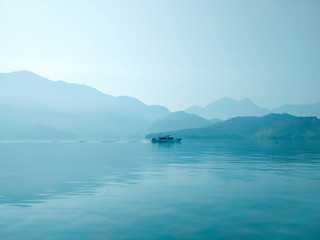 Fototapeta na wymiar Large blue lake with lonely ship in the morning