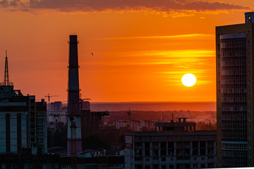 Fototapeta na wymiar Sunset in big city. White sun and orange sky among high-rise city buildings. White clouds glow in rays of setting sun. Close-up. Voronezh, Russia, June 2019.