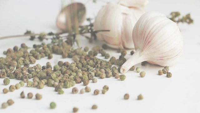 Green peppercorns - pepe verde - famous spice of Italian cuisine on white table with garlic bulbs, thyme twig and spoon. Pouring green peppercorns on white table. Foggy background.
