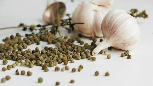 Green peppercorns - pepe verde - famous spice of Italian cuisine on white table with garlic bulbs, thyme twig and spoon. Pouring green peppercorns on white table.