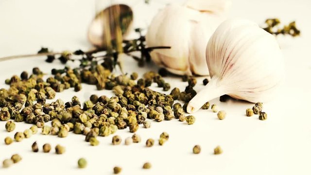 Green peppercorns - pepe verde - famous spice of Italian cuisine on white table with garlic bulbs, thyme twig and spoon. Pouring green peppercorns on white table.