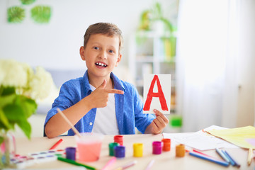 happy child at the table with school supplies smiles funny and learns the alphabet in a playful...