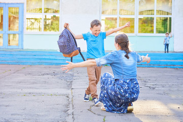 mom meets her son from elementary school. joyful child runs into the arms of his mother. a happy schoolboy runs towards his mother holding a school bag in his hands.