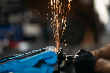 Worker cutting, grinding and polishing motorcycle metal part with sparks indoor workshop, close-up.